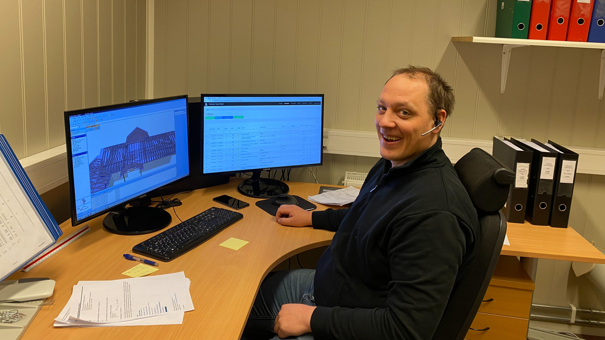 bildet viser en mann som sitter foran to dataskjermer på kontoret og smiler